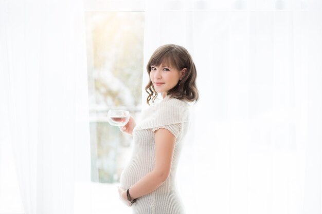 Happy young pregnancy standing near a window at home