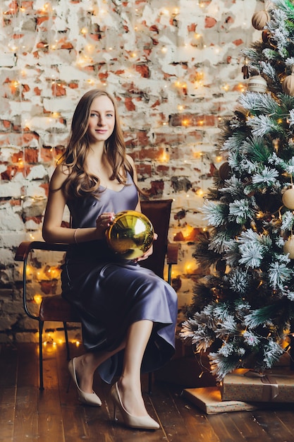 Happy young pregnant woman sitting near the Christmas tree.