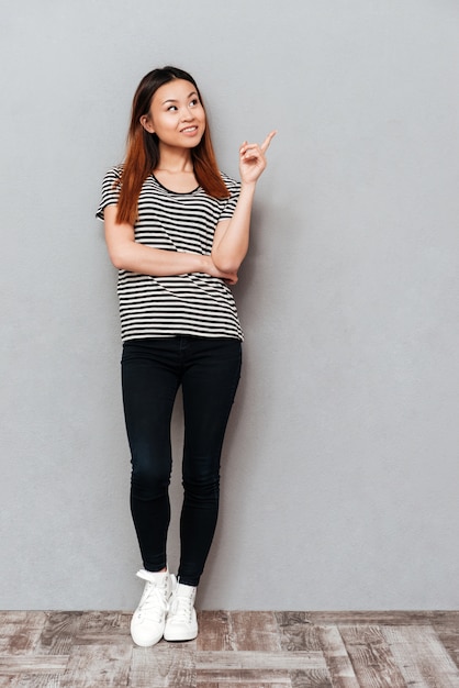 Happy young pretty woman standing over grey wall.