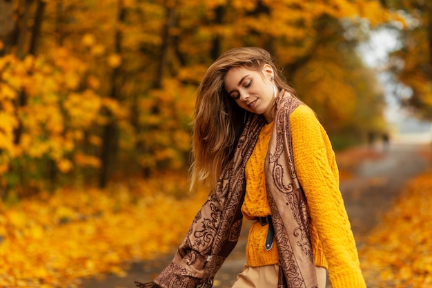 Happy young pretty woman with scarf in vintage knitted yellow sweater walking in the park with autumn yellow foliage