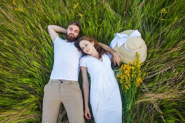 Happy young relaxed couple in love laying down on the grass overhead