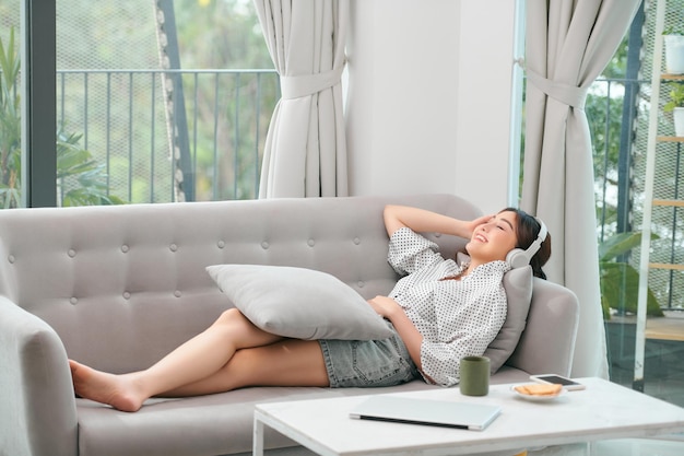 Happy young relaxed woman with headphones sitting on couch and listening to meditation music at leisure