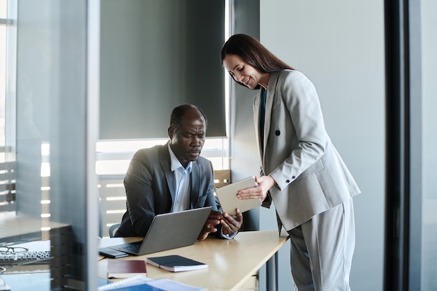 happy young secretary with tablet bending over workplace of her boss