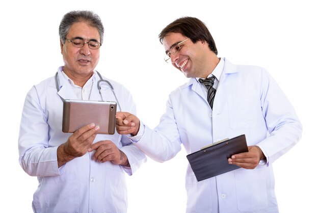 happy young and senior Persian man doctor smiling and holding digital tablet and clipboard