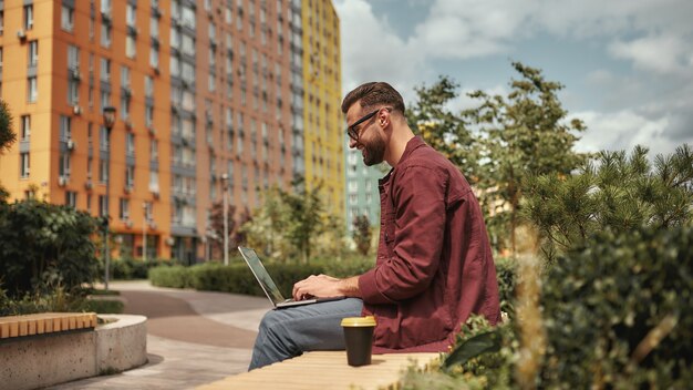 Happy and young side view of handsome man with stubble in casual clothes and eyeglasses