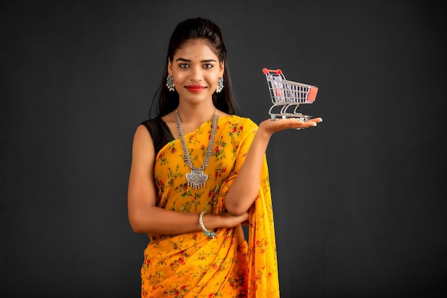 Happy young Smiling girl with a miniature trolley shopping cart on the gray background Beautiful girl in shopping concept