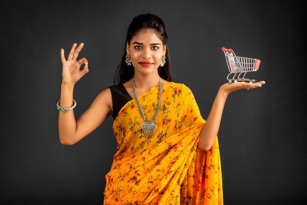 Happy young Smiling girl with a miniature trolley shopping cart on the gray background Beautiful girl in shopping concept