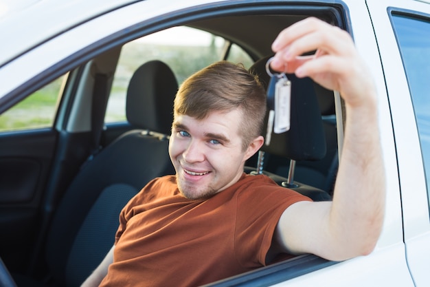 キーと新しい車の中に座っている幸せな若い笑顔の男。