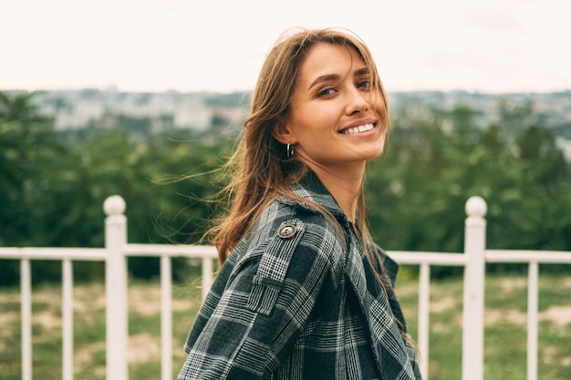 Foto felice giovane donna sorridente che indossa il cappotto sta camminando all'aperto per le strade della città in una giornata ventosa