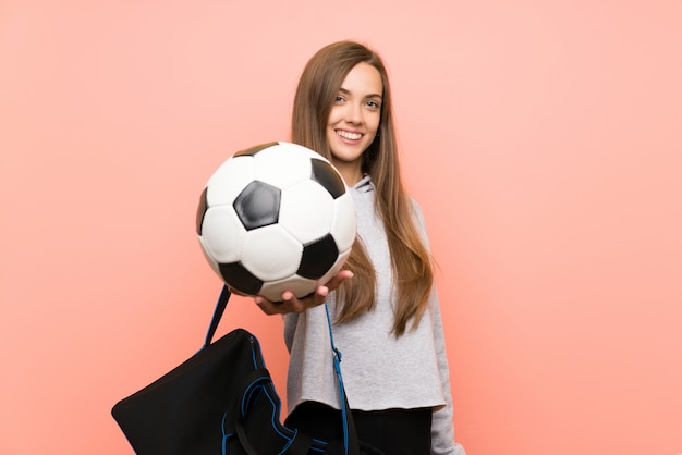 Happy Young sport woman over isolated pink holding a soccer ball