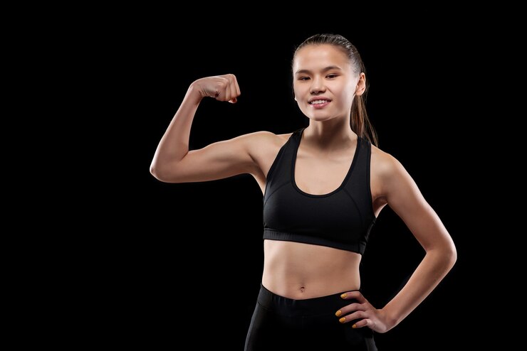 Photo happy young sportswoman in black activewear looking at you while showing her physical strength and muscles