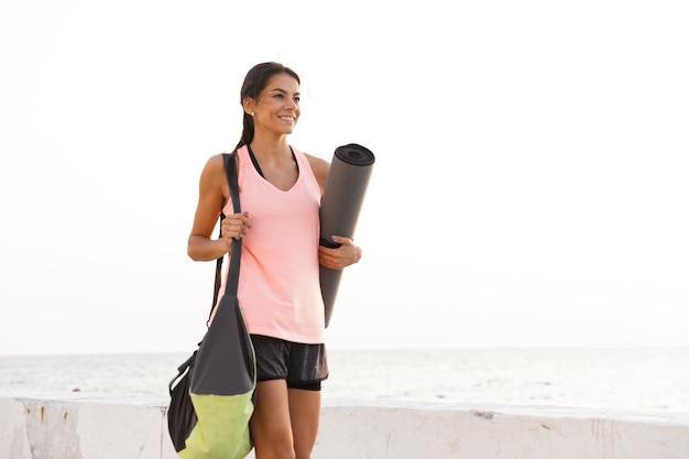 Happy young sportswoman holding fitness mat