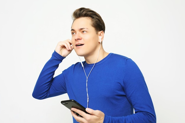 Happy young stylish man adjusting his headphones and smiling while standing against white background