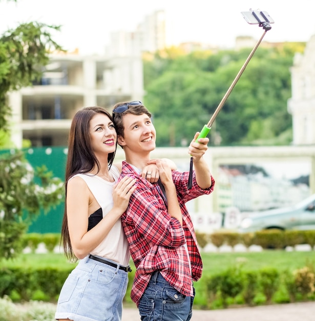 Happy young tourists couple taking a selfie with smartphone on the monopod in city the man is