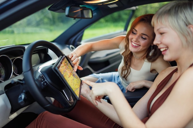 Photo happy young two women driver tourist travelers with digital tablet pad map at rental car vehicle