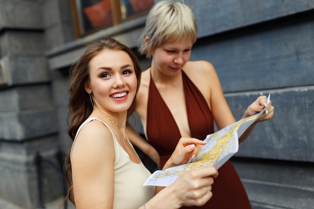 Happy young two women tourist travelers with paper map is exploring new city