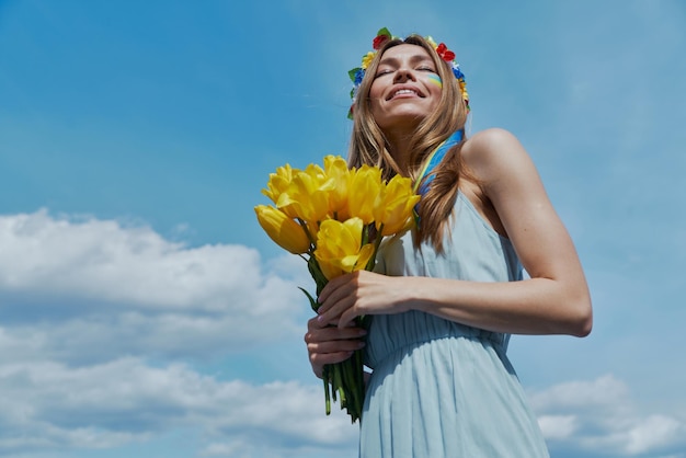 背景に青い空の黄色いチューリップを持った花の冠をかぶった幸せな若いウクライナの女性