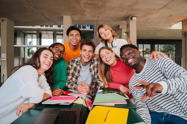 Foto giovani studenti universitari felici che sorridono e guardano la telecamera divertendosi insieme seduti nel