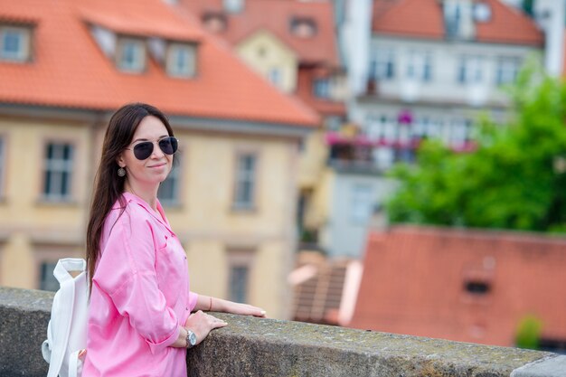 Giovane donna urbana felice in città europea sul ponte famoso. turista caucasico che cammina lungo le strade deserte d'europa. calda estate mattina presto a praga, repubblica ceca