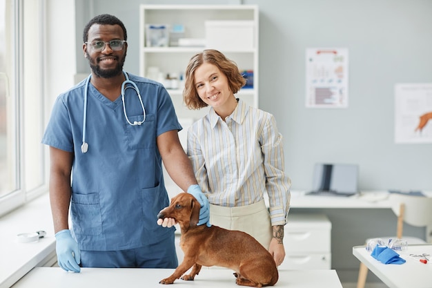 Happy young veterinarian and pet owner standing by medical table