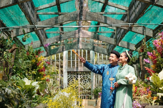 Photo happy young vietnamese man showing beautiful flowers in greenhouse to bride