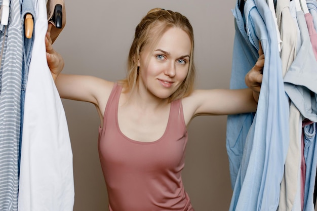 Photo happy young white woman looks out from behind clothes hanging on a hanger smiles at the camera is