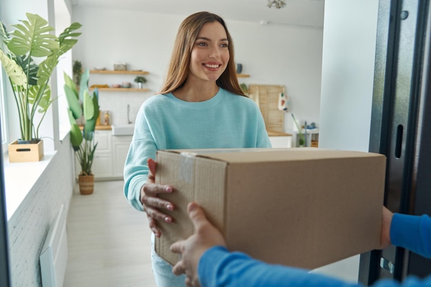 happy young woman accepting box from delivery man at home