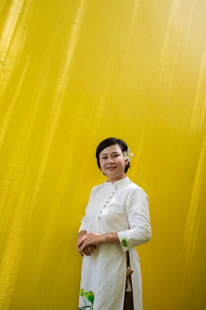 Happy young woman in ao dai dress standing outdoors at the yellow wall