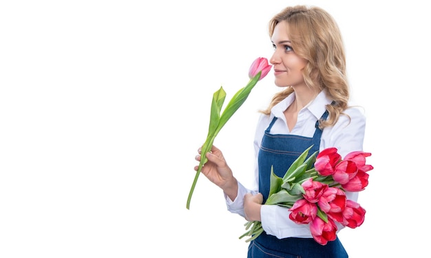 Счастливая молодая женщина в фартуке пахнет весенними цветами тюльпанов на белом фоне