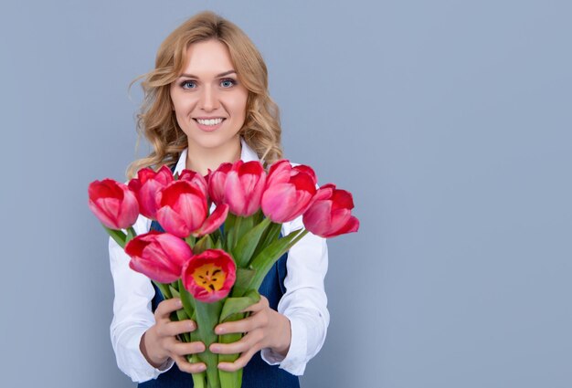 灰色の背景に春のチューリップの花とエプロンで幸せな若い女