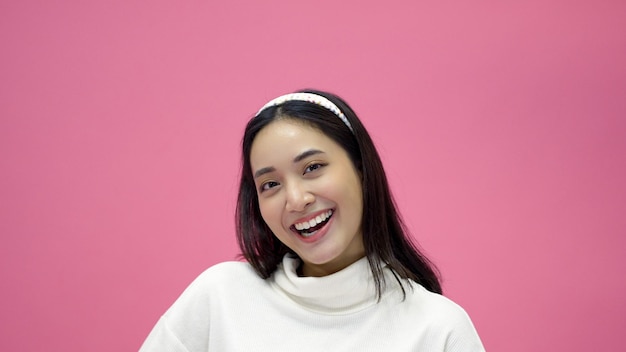 Счастливая молодая женщина-азиатка улыбается и хорошо проводит время, смеясь, глядя в сторону на розовом фоне