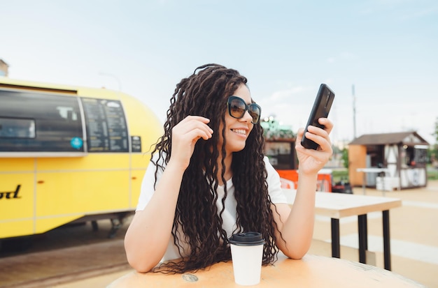 A happy young woman attending a web conference through\
headphones or a freelancer sitting at an outdoor cafe table a girl\
with dreadlocks communicates via video link
