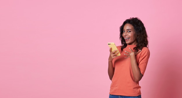Happy young woman being surprised after reading message from smartphone isolated over pink
