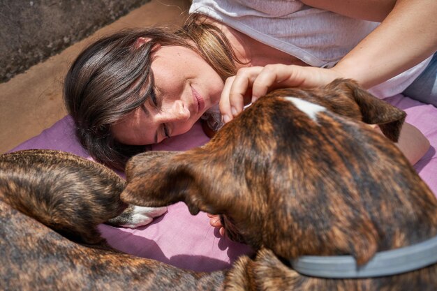 Happy young woman caressing pet with tenderness while resting on wooden floor at home