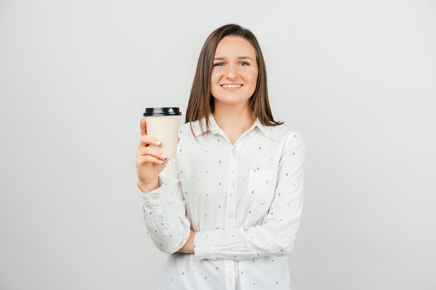 Giovane donna felice in tazza di caffè di carta della tenuta casuale per andare e che esamina la macchina fotografica