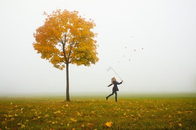 Happy young woman catching autumn leaves with net