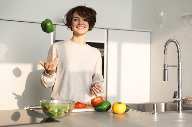 Happy young woman cooking fresh salad at the kitchen at home