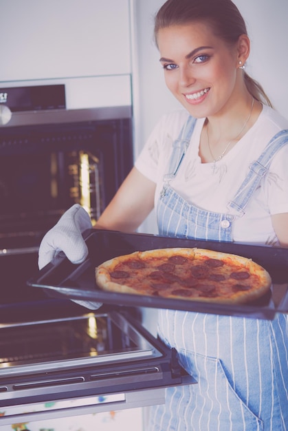 Felice giovane donna che cucina pizza a casa