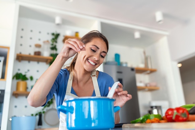 Happy Young Woman Cooking Tasting Dinner In A Pot Standing In Modern Kitchen At Home Housewife Preparing Healthy Food Smiling Household And Nutrition Dieting Recipes Concept