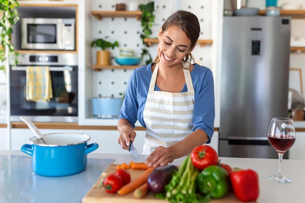 Happy young woman cooking tasting dinner in a pot standing in\
modern kitchen at home housewife preparing healthy food smiling\
household and nutrition dieting recipes concept