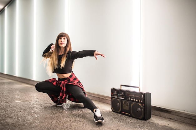 Happy young woman dancing and sitting in the street with a vintage radio cassette stereo xA