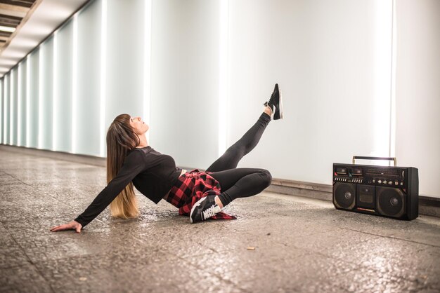 Happy young woman dancing and sitting in the street with a
vintage radio cassette stereo xa