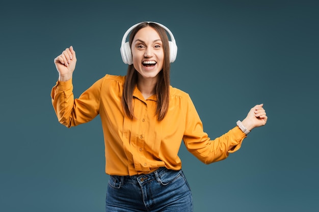 ハッピーな若い女性がヘッドフォンをかぶって踊りカメラを見ながら音楽を聴いています