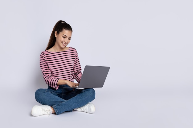 Happy young woman digital nomad using laptop grey background