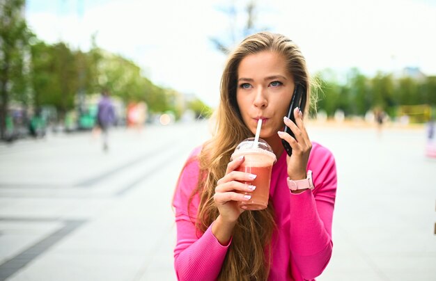 Felice giovane donna che beve un caffè all'aperto mentre parla al telefono