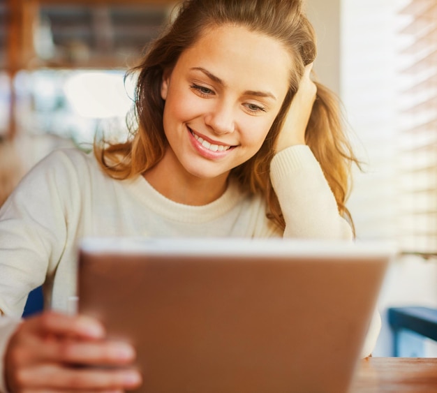 Giovane donna felice che beve caffè e tè e usa un tablet in un caffè