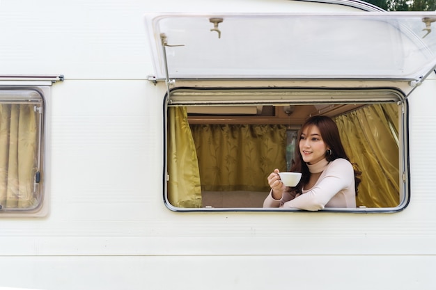 Happy young woman drinking coffee at window of a camper RV van motorhome