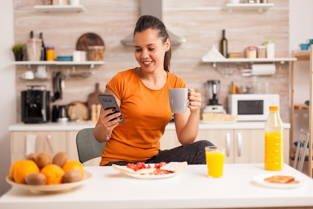 Happy young woman drinking a cup of coffee and use her phone to read the news