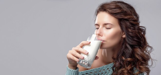 Happy young woman drinking milk over grey space