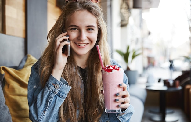 スムージーを飲み、携帯電話のsmで話している幸せな若い女性